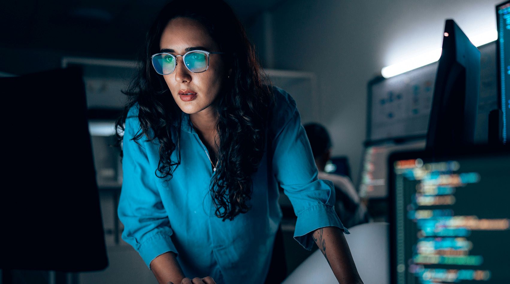 cybersecurity professional looking at computer monitor in dimly lit room
